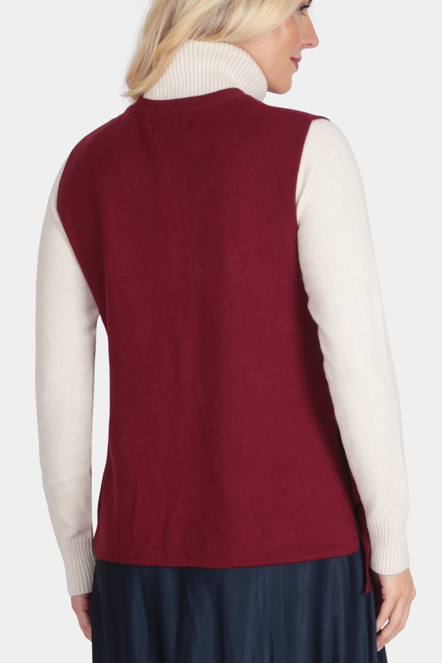 Woman wearing a red vest over a white shirt and navy skirt on a white background