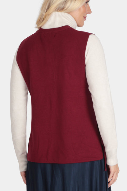 Woman wearing a red vest over a white shirt and navy skirt on a white background